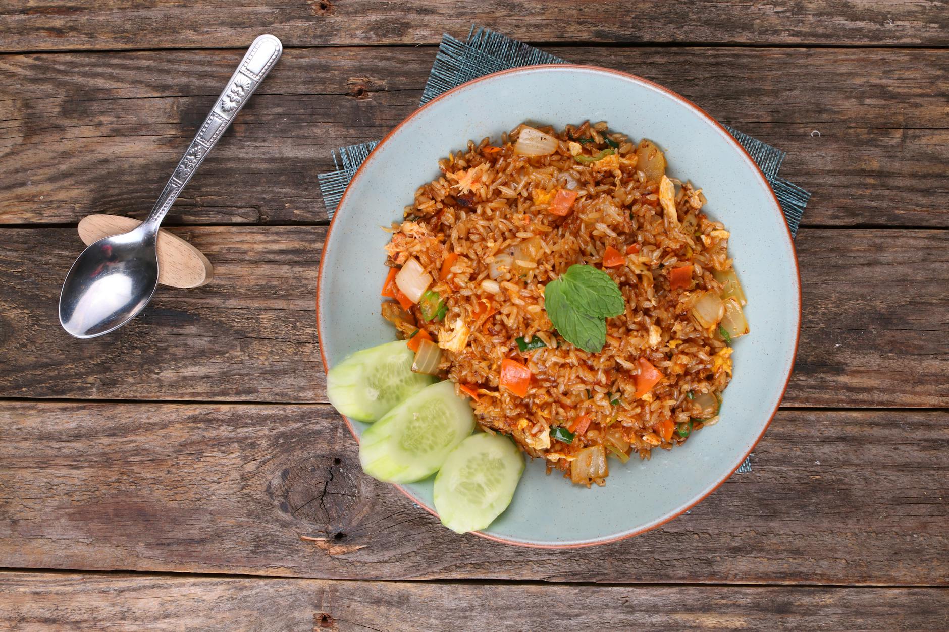 Miska chińskiego ryżu smażonego z warzywami i ogórkiem na drewnianym stole