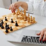 Osoba przy laptopie zagrywa pionkiem na szachownicy