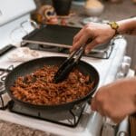 Dłonie mieszają mięso na tacos w patelni na kuchence gazowej