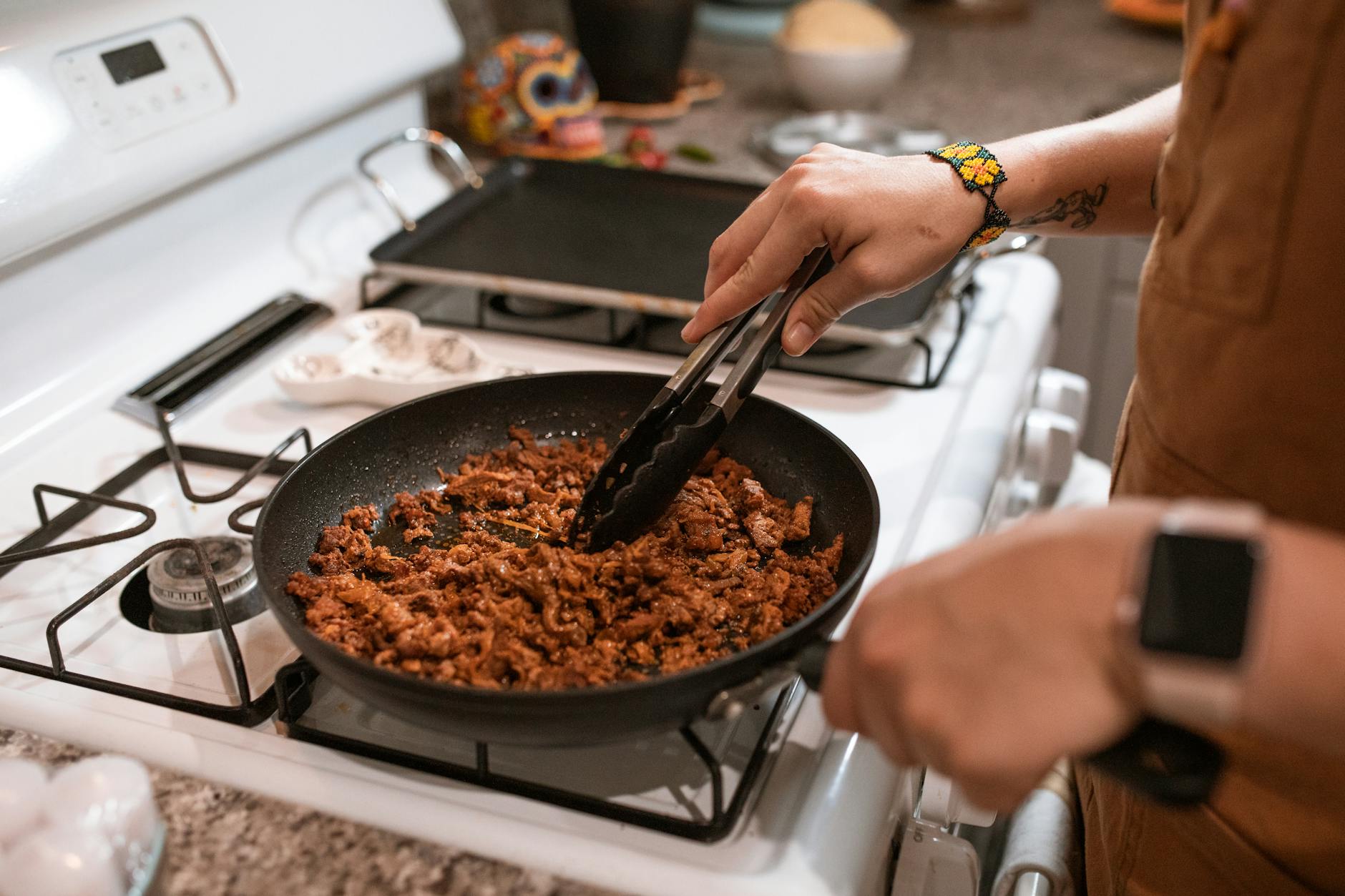 Dłonie mieszają mięso na tacos w patelni na kuchence gazowej