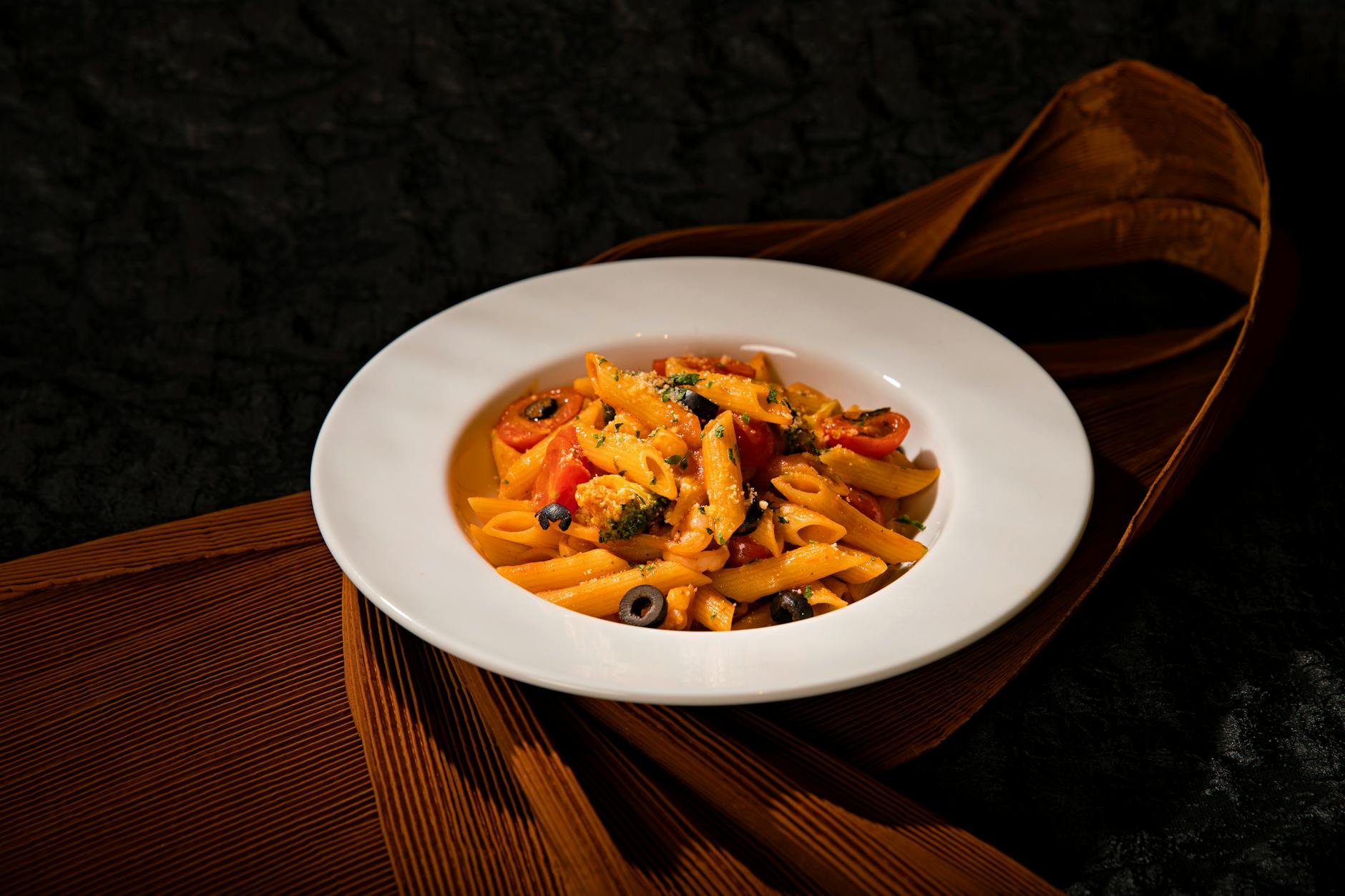 Makaron penne z kolorowymi warzywami na białym talerzu na ciemnym tle