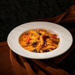 Makaron penne z suszonymi pomidorami i oliwkami na białym talerzu