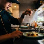 Szef kuchni posypuje przyprawą elegancko podane danie w restauracyjnej kuchni