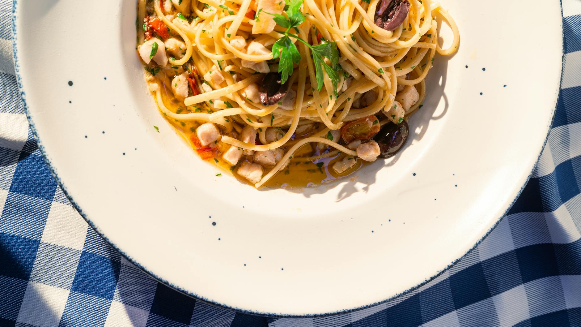 Talerz spaghetti z owocami morza i oliwkami na kraciastym obrusie